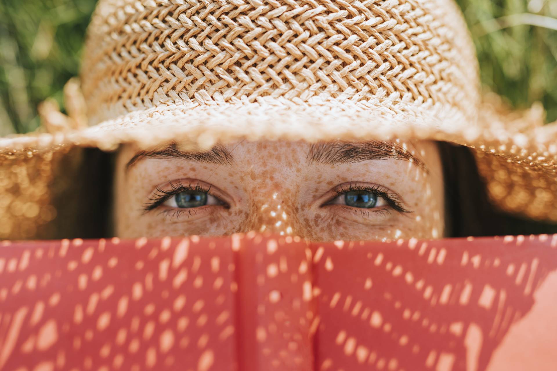 Closeup of woman covering her face with a red book